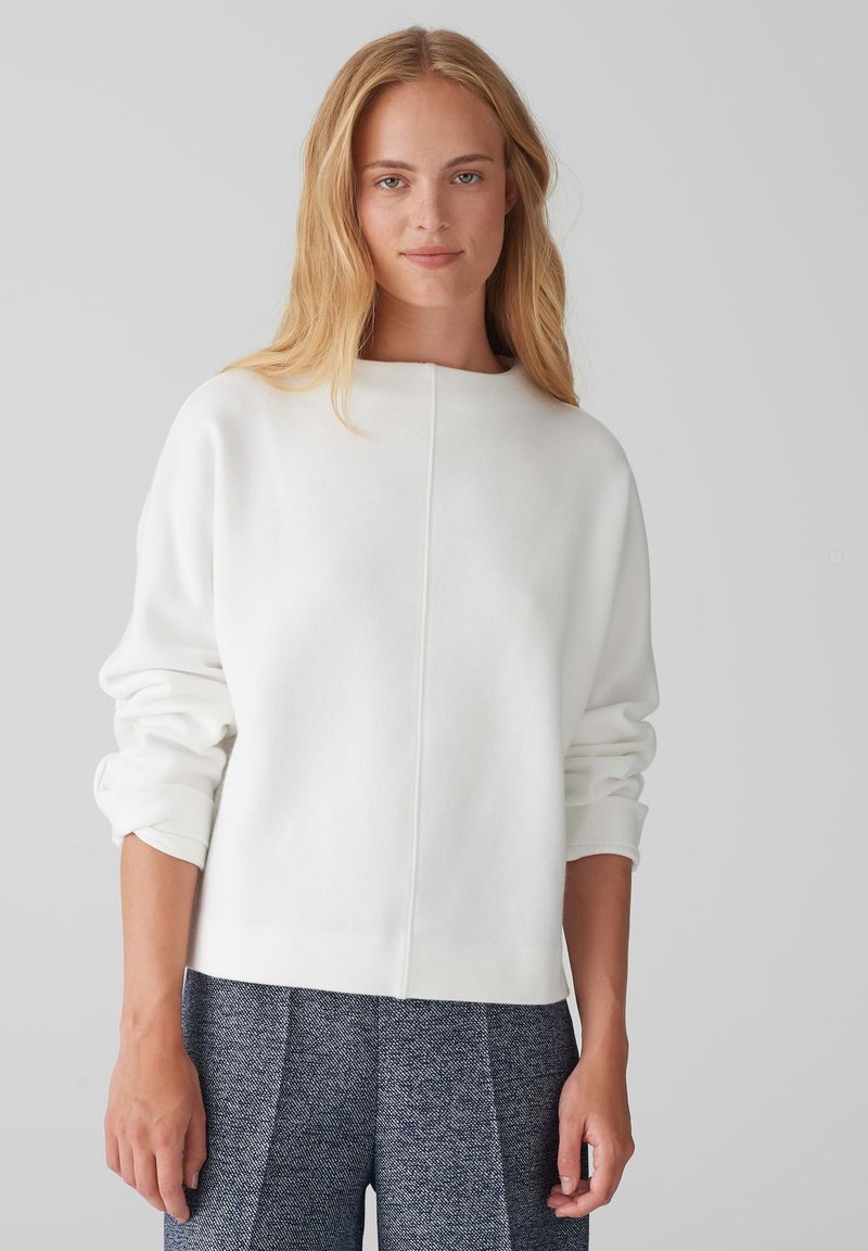 White sweatshirt with a crew neck, dropped shoulders, and ribbed cuffs. Smooth texture, minimal seams, paired with textured blue patterned pants.