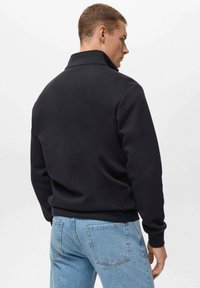Zwarte fleece sweatshirt met een hoge kraag, geribbelde manchetten en een relaxte pasvorm, gecombineerd met lichtblauwe spijkerbroek.