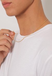 Collana a catena d'oro tenuta in mano, caratterizzata da una trama fine e un design delicato, indossata con una semplice maglietta bianca.