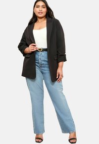 Melna žakete ar sarullētām piedurknēm, balta blūze, augstās izgriezuma gaiši zilas džinsus un melnas sandaļbikses. Bieza zelta josta ar sprādzi.