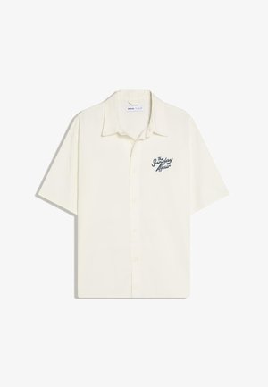 Kremasta košulja kratkih rukava s ovratnikom i tekstom "The Sunday Affair" na lijevoj strani prsnog dijela.