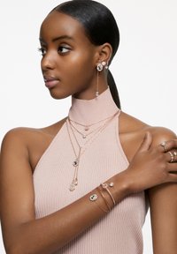 Las joyas de oro rosado incluyen collares en capas con colgantes circulares, pendientes a juego con acentos colgantes y anillos con detalles adornados.