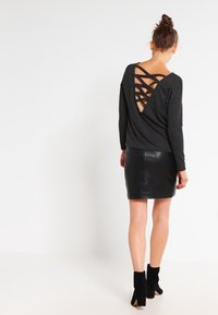 Top nero a maniche lunghe con scollatura a V e retro aperto, caratterizzato da spalline incrociate; abbinato a una mini gonna in pelle nera e stivaletti alla caviglia.