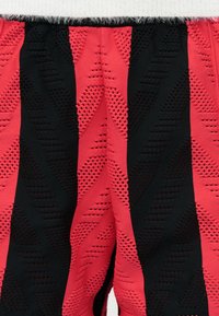 Κοντινή λήψη υφάσματος πλεκτού με ανάγλυφα κάθετα κόκκινα και μαύρα ριγέ, που διαθέτουν ανυψωμένα τριγωνικά σχέδια.