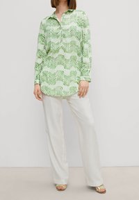 Camicia a maniche lunghe verde e bianca con un motivo a foglie abbinata a pantaloni bianchi. Il tessuto ha una consistenza leggera e liscia.