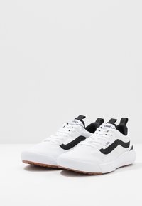 White sneakers with a mesh upper, black side stripe, and rubber outsole. Features include traditional laces and pull tabs on the heel.