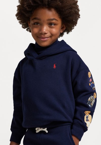 Ναυτικού μπλε φούτερ από βαμβάκι, με κόκκινο λογότυπο στο στήθος και σχέδια αρκούδων στα μανίκια. Μαλακή υφή, άνετη εφαρμογή.