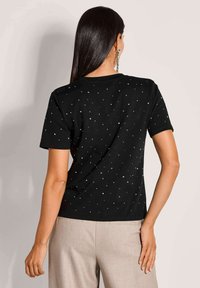 Zwarte T-shirt met korte mouwen, met verspreide metalen studs. Een gladde textuur en een klassieke pasvorm, met een ronde hals en een effen zoom.