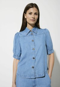 Hellblaues Jeanshemd mit kurzen Puffärmeln, einem Kentkragen und Metallknöpfen auf der Vorderseite. Lässiger Schnitt mit geradem Saum.