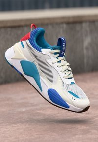 Sapatilha branca com detalhes em azul e vermelho, parte superior em malha com painéis texturizados, sola almofadada e sistema de atacadores para um ajuste seguro.