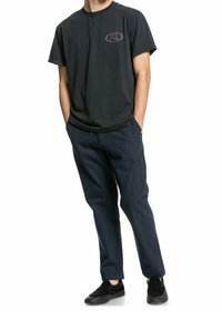 Svart bomull t-shirt med en cirkulär logotyp; ihopparad med marinblå randiga byxor. Skorna är svarta slip-on med platt sula.