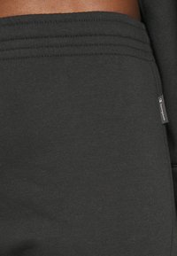 Pantalones de chándal negros de algodón con una textura suave, cintura elástica con acentos acanalados y una pequeña etiqueta de logo en el costado.