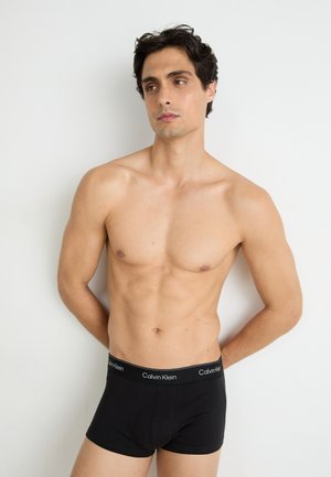 Schwarze Baumwoll-Boxershorts mit einem elastischen Bund mit Logo, dargestellt an einer shirtlosen männlichen Figur vor einem hellen Hintergrund.