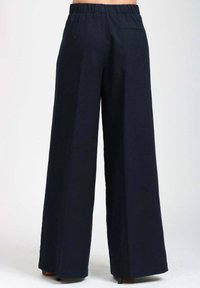 Pantaloni a gamba larga blu navy con vita elasticizzata e una tasca sul retro indossati da una persona in piedi di spalle.