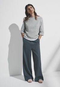 Grå strikket sweater med trekvartlange ærmer, parret med mørke stribede bukser med brede ben og lyserøde slip-on sko.