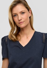 Navyblauw V-hals top met korte pofmouwen met kantdetails op de schouders, gemaakt van een zachte, gestructureerde stof.