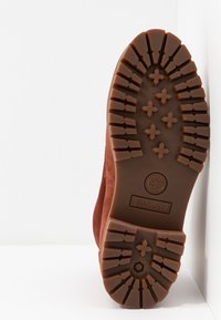 Semelle marron de botte Timberland montrant un motif de bande de roulement profond et un logo embossé sur fond blanc.