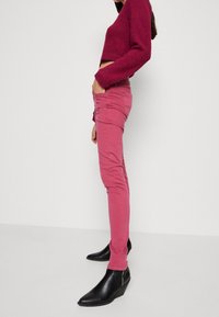 Pantalones rosa ajustados hechos de suave algodón, con una textura lisa. Combinados con botas de tobillo de cuña negras para aportar contraste.