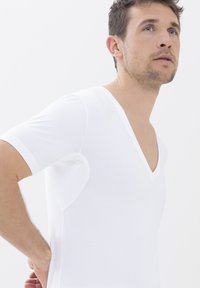 Weißes Kurzarmhemd mit tiefem V-Ausschnitt. Weicher Stoff mit glatter Textur. Verfügt über seitliche Einsätze für Komfort und ein tailliertes Design.