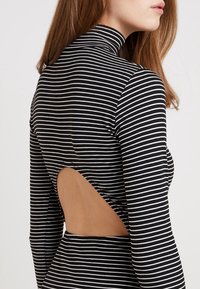 Raitaraitainen musta-valkoinen pitkähiha dressi, jossa on korkea kaula-aukko ja avoin selkäosa, on valmistettu sileästä ja joustavasta kankaasta.