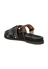 Sandal nera con due cinturini regolabili, borchie decorative e una soletta imbottita. Presenta una suola marrone e un design piatto.