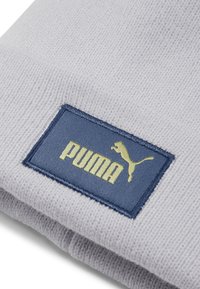 Svijetlosiva pletena kapa s plavom tkaninom s žutim logotipom "PUMA" i siluetom mačke, s rebrastom teksturom na tkanini.