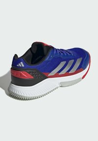 Baskets de sport bleues et rouges avec une tige en mesh, des rayures argentées, des accents noirs et une semelle en caoutchouc blanc avec un motif texturé.
