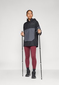 Letvægts sort og grå jakke med hætte, der har en skrå frontlomme; parret med bordeaux leggings og sorte vandrestøvler.
