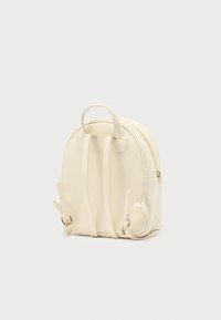 Σακίδιο πλάτης από κρεμ τεχνητό δέρμα με στρογγυλεμένο σχήμα, διπλούς ιμάντες ώμου, κλείσιμο με φερμουάρ και ανάγλυφη λεπτομέρεια στο πλάι.