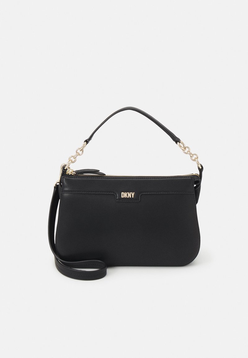 Sac à main noir DKNY avec poignée accentuée de chaîne en or, fermeture éclair sur le dessus et bandoulière détachable sur fond clair uni.