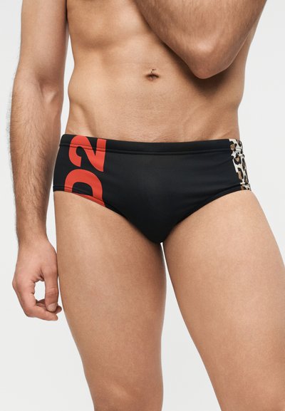 Ανδρικός κορμός που φοράει μαύρο μαγιό σλιπ με κόκκινο κείμενο "D2" στην αριστερή πλευρά και λεπτομέρεια λεοπάρ στην δεξιά πλευρά.