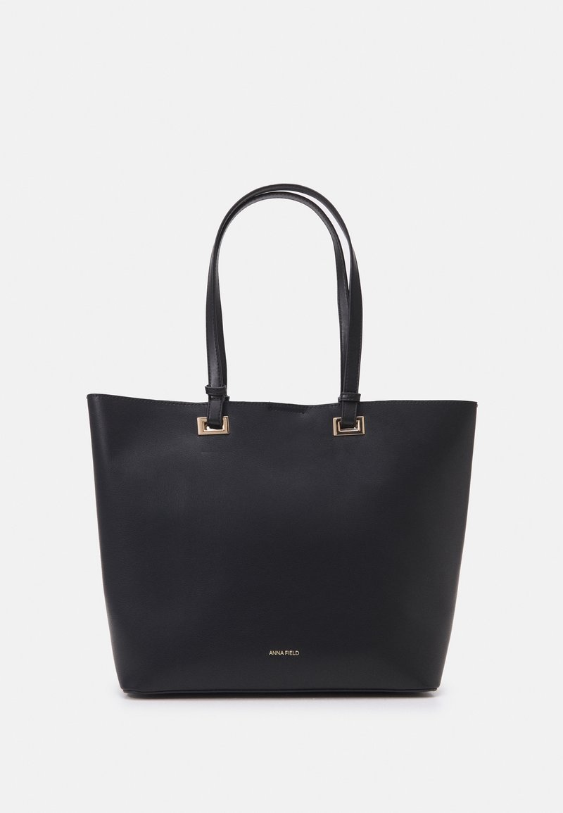 Sac cabas en cuir noir avec deux longues anses et une quincaillerie dorée, avec un petit logo "ANNA FIELD" sur le devant.