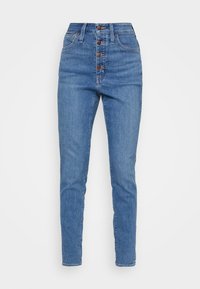 Jeans de mezclilla azul de talle alto con cierre frontal de cinco botones, corte ajustado y ligero desgastado en los muslos. Diseño clásico de cinco bolsillos.