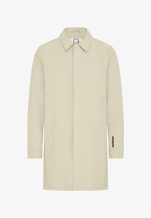 Beige pitkähiha, jossa on kaulus, etutaskut ja suora leikkaus. Ominaisuuksiin kuuluu minimaalinen ompelu ja vasemmassa hihassa sijaitseva etiketti.