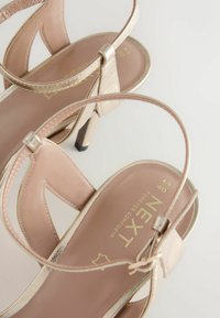 Le sandali con tacco nudi presentano un design a fasce incrociate in pelle liscia, dettagli metallici e solette imbottite, ideali per comfort ed eleganza.