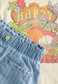 Pantalones cortos de algodón a rayas azul claros con cinturilla con volantes y detalle de botones, combinados con una camiseta gráfica retro colorida que presenta flores y mariposas.