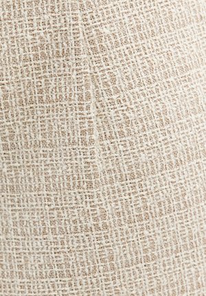 Tissu tissé beige et blanc cassé avec un motif texturé en croisillons et une couture visible.