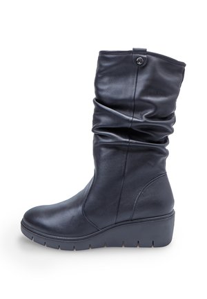 Črne čevlje z vzpeto peto do polovice meč iz slušnega usnja, okrogla konica in z detajlom gumbaste zaponke blizu vrha na beli podlagi.