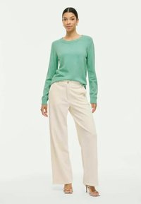 Suéter verde claro de manga larga combinado con pantalones anchos color crema. La ropa presenta un diseño sencillo y una textura suave.