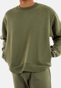 Sudadera verde oliva hecha de una mezcla de algodón, con cuello redondo, puños acanalados y dobladillo. Diseño simple sin patrones ni acentos.