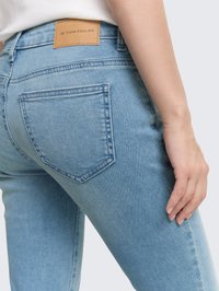 Zbližnja slika osebe, ki nosi svetlo modre Tom Tailor jeans, s prikazom zadnjega žepa in oznake blagovne znamke na pasu.