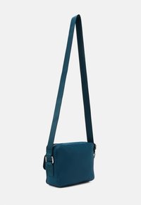 Borsa a tracolla turchese realizzata in tessuto liscio, con forma rettangolare, tracolla regolabile e dettagli in metallo argentato. Chiusura con zip.