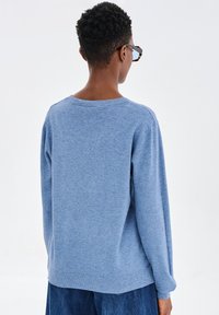 Niebieski sweter dzianinowy z długimi rękawami, okrągłym dekoltem i ściągaczem na dole. Miękka tekstura i luźny krój. Noszony z dżinsowymi spodniami.