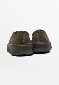 Baskets en suede marron avec une silhouette basse, bout arrondi et un subtil détail de coutures. Semelle en caoutchouc durable avec une texture antidérapante. Vue arrière affichée.