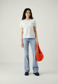 Λευκό βαμβακερό μπλουζάκι με μικρή πράσινη και κίτρινη κεντημένη floral διακόσμηση, συνδυασμένο με ανοιχτό μπλε τζιν με καμπάνα και πορτοκαλί τσάντα με υφή.