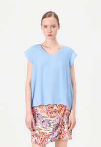 Blusa azzurro chiaro a maniche corte con scollatura a V, realizzata in tessuto testurizzato, abbinata a una gonna multicolore con un motivo vivace.