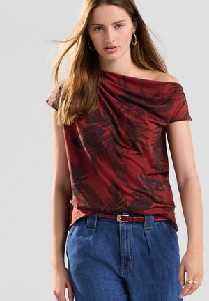 Rode off-the-shoulder t-shirt met een donkere bladerenpatroon, gecombineerd met hoge taille spijkerbroeken en een bijpassende rode riem. Gladde textuur, casual stijl.