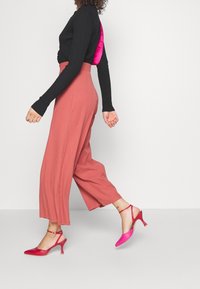 Zwarte lang-sleeve top met een roze satijnen achterkant, gecombineerd met roze wijde broek en roze slingback hakken met een spitse neus.
