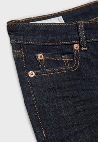 Jean en denim foncé avec des rivets en cuivre visibles, des coutures orange contrastantes et une poche avant. L'étiquette indique la taille 36. Vue à plat.