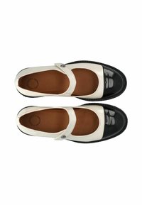Zapatos Mary Jane de cuero con un empeine blanco, puntera negra brillante, correa de tobillo con un botón y una suela negra texturizada.